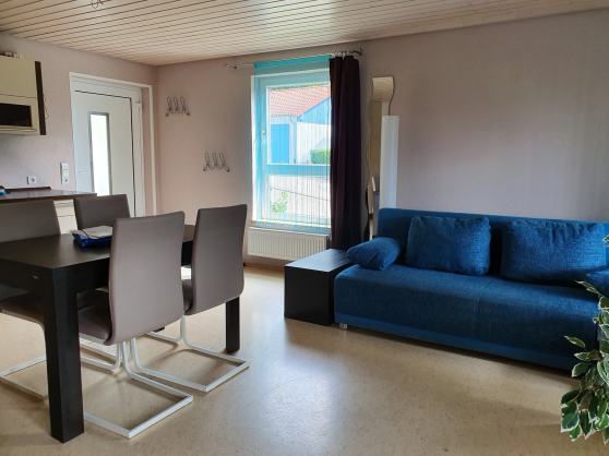 Links Tisch und Essplatz für 4 Personen, dahinter eine Küchenzeile, rechts ein Sofa